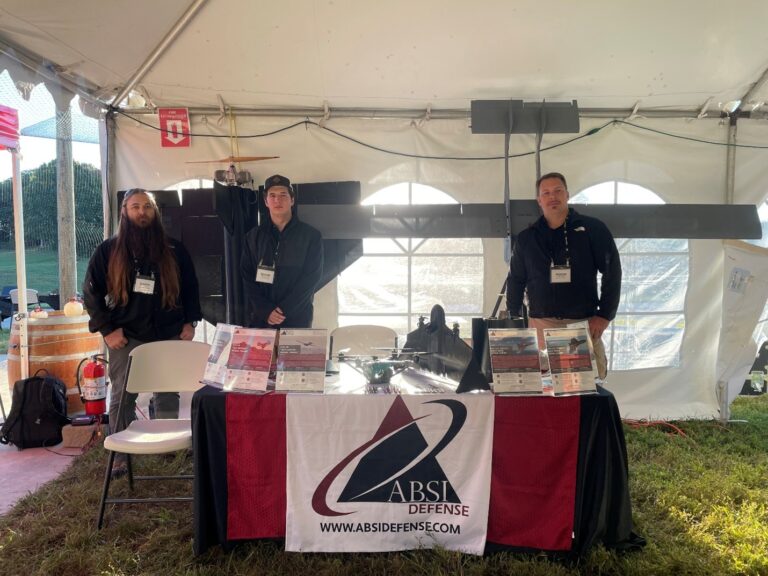 ABSI team at the booth with the SkyBadger platform with Remora, RATTLER and Nomad in the background.)
